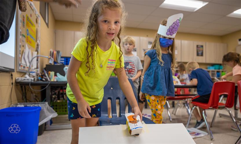 A girl smiles while releasing a toy car down a ramp
